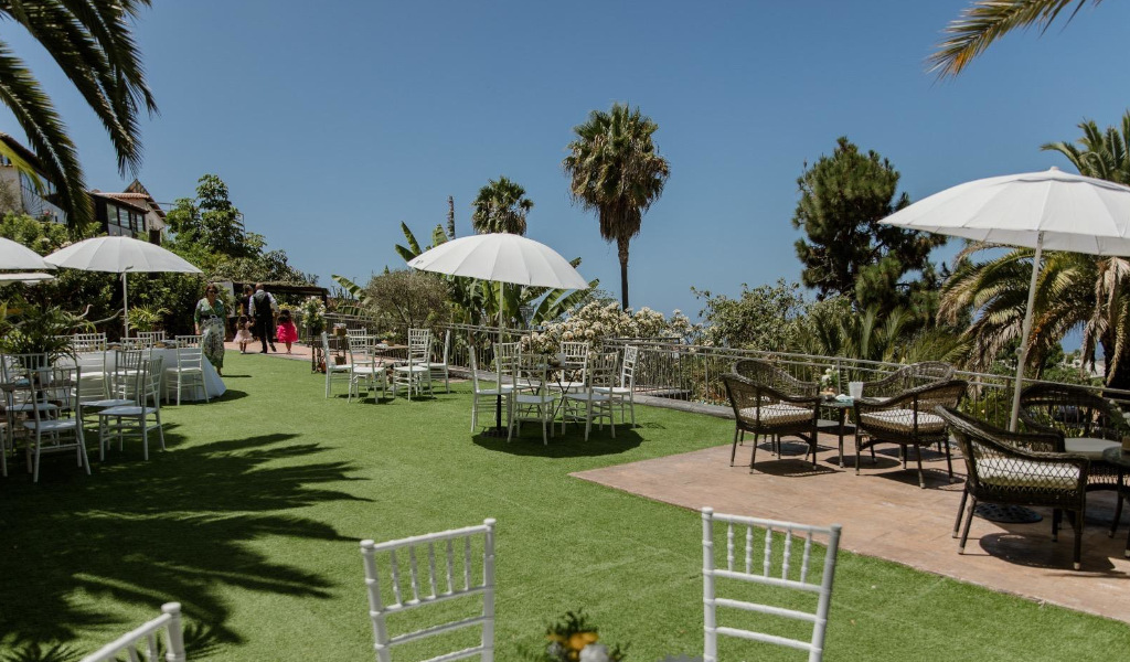 Terraza con sillas blancas, parasoles y palmeras en un jardín de Tenerife.