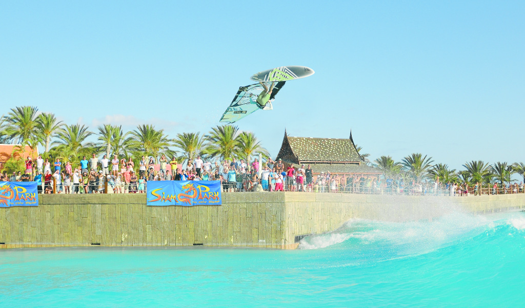 Surfista saltando en piscina de olas en Siam Park, Tenerife, bajo cielo despejado.