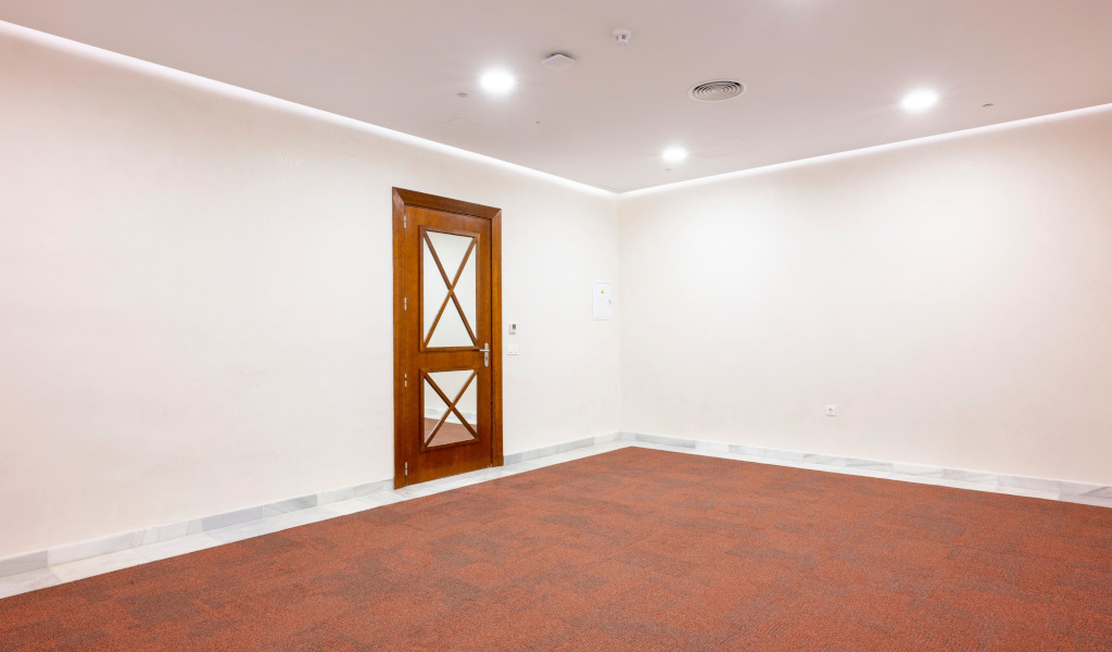 Sala vacía con puerta de madera y alfombra roja en centro de conferencias en Tenerife.