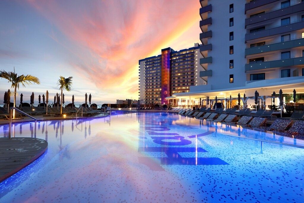 Piscina iluminada al atardecer en hotel de Tenerife, rodeada de tumbonas y palmeras.