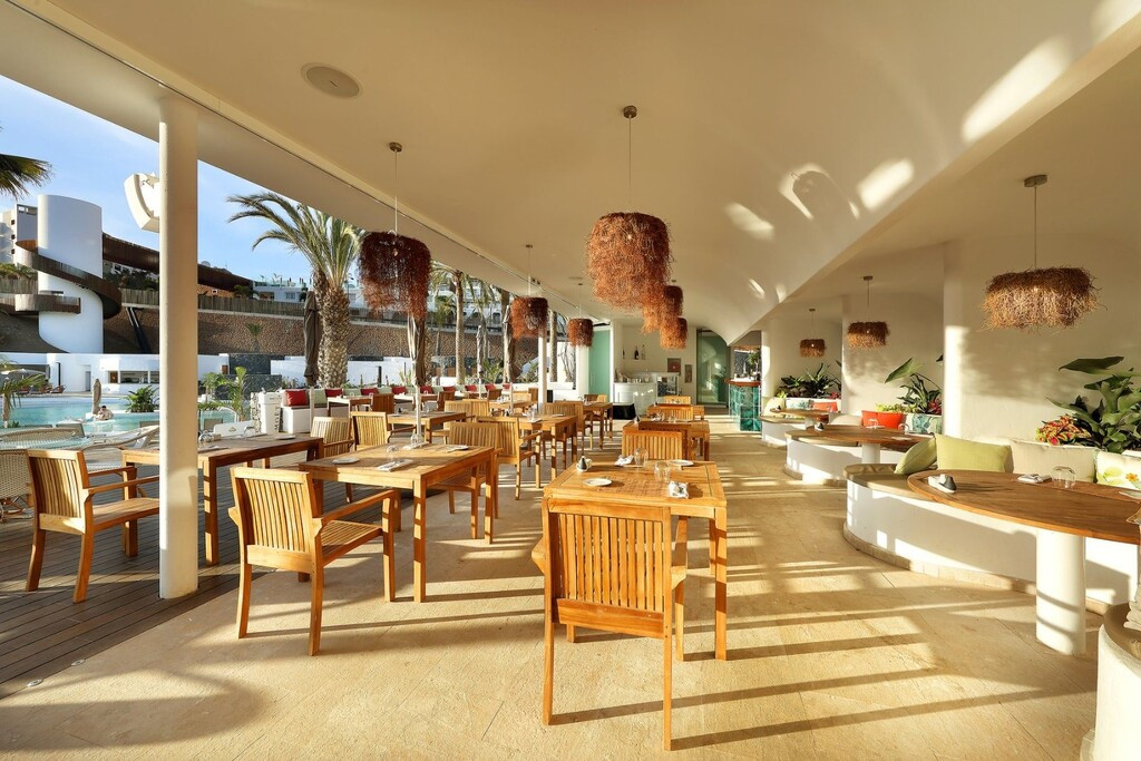 Restaurante al aire libre con sillas de madera y vistas a la piscina en Tenerife.