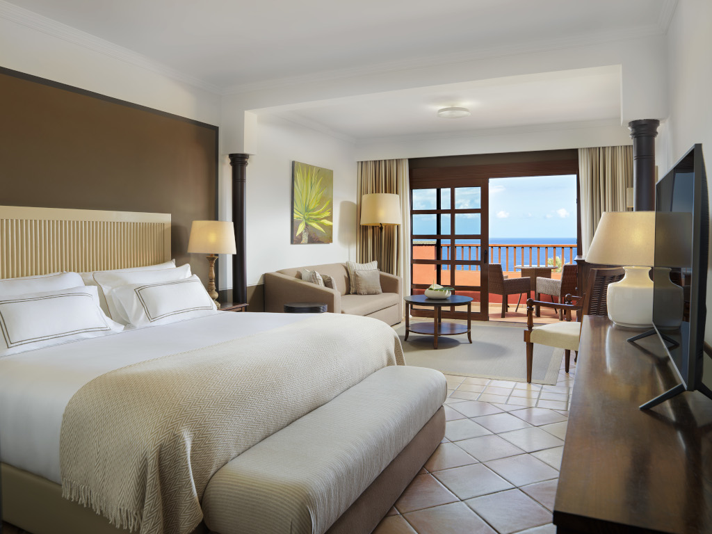 Habitación de hotel en Tenerife con cama, sala de estar y balcón con vista al mar.