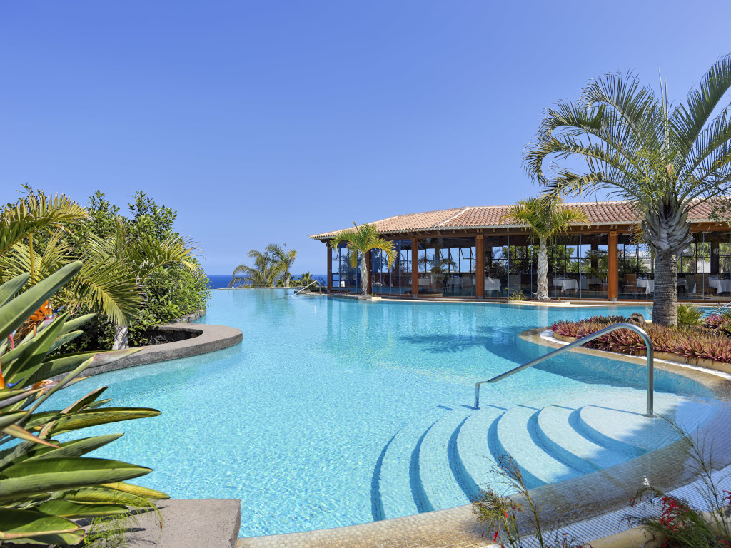 Piscina rodeada de palmeras y restaurante en Tenerife.