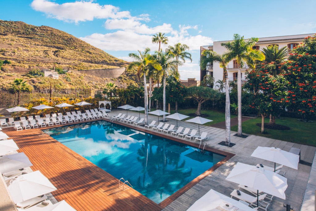 Piscina rodeada de tumbonas y sombrillas, con montañas al fondo en Tenerife.