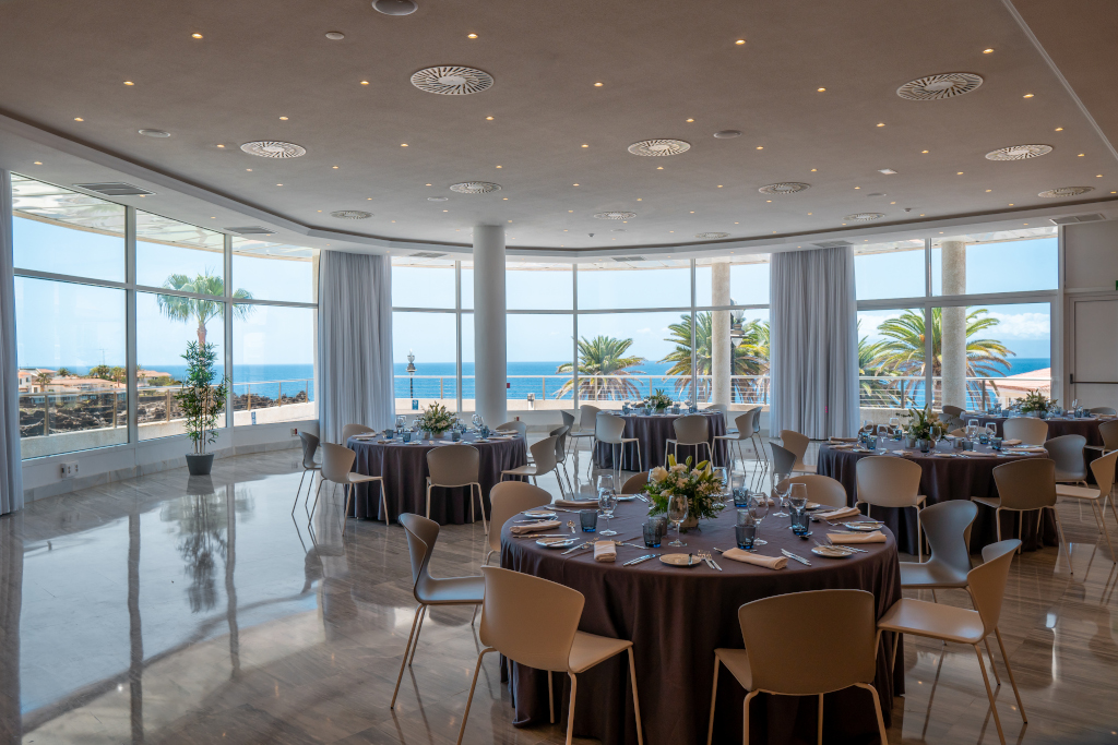 Salón de eventos con mesas redondas y vista al mar en Tenerife.