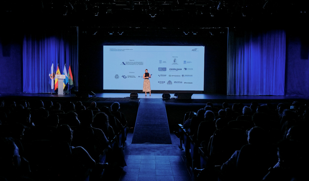 Persona en escenario durante conferencia en lugar de Tenerife, con proyección de logotipos.