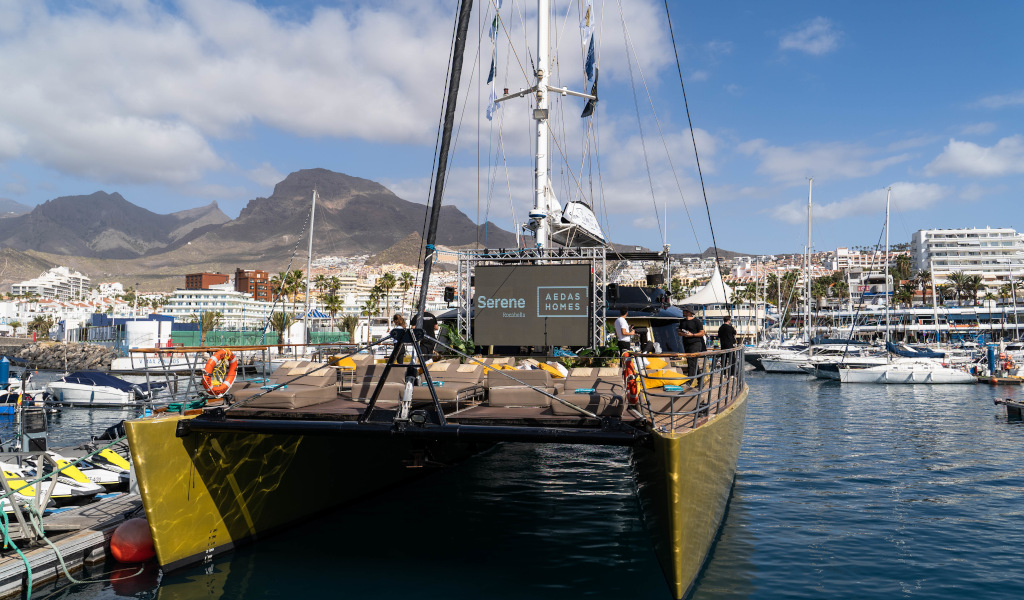 Catamarán atracado en puerto deportivo en Los Cristianos, Tenerife, con montañas al fondo.