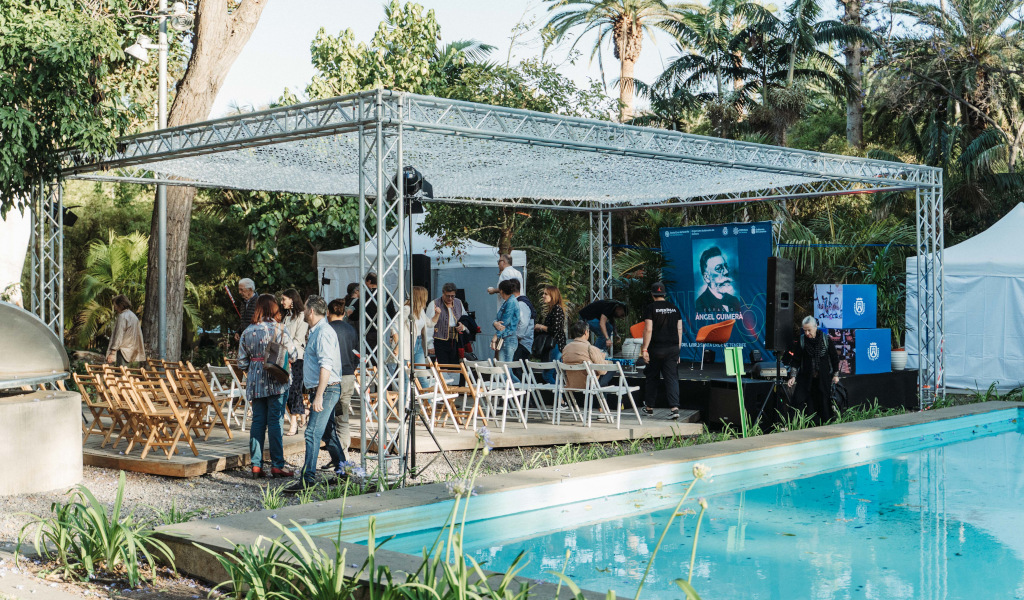 Evento en un jardín de Tenerife con asientos y cartel de Ángel Guimerá cerca de una piscina.