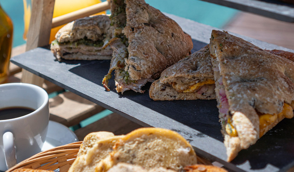Sándwiches de jamón y queso sobre tabla, con taza de café, en una terraza de Tenerife.