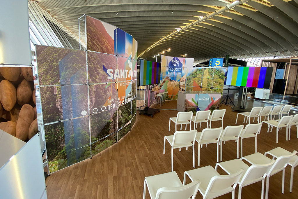 Stands promocionales de Santa Cruz en un centro de eventos con sillas blancas.