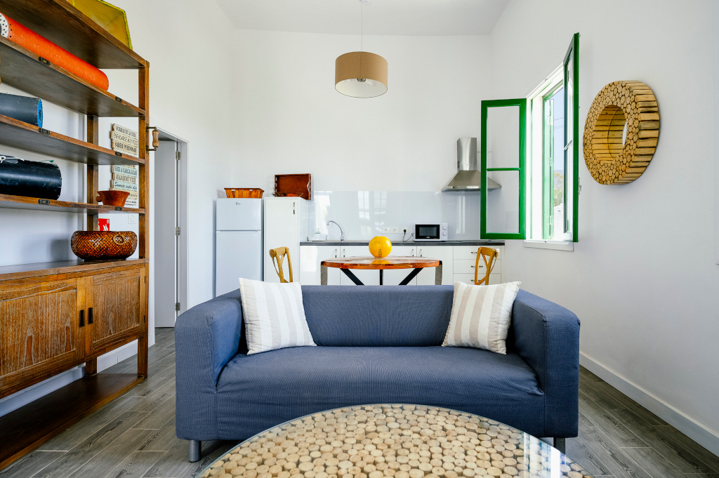 Sala de estar con cocina abierta, sofá azul, mesa de centro y ventana verde en Tenerife.
