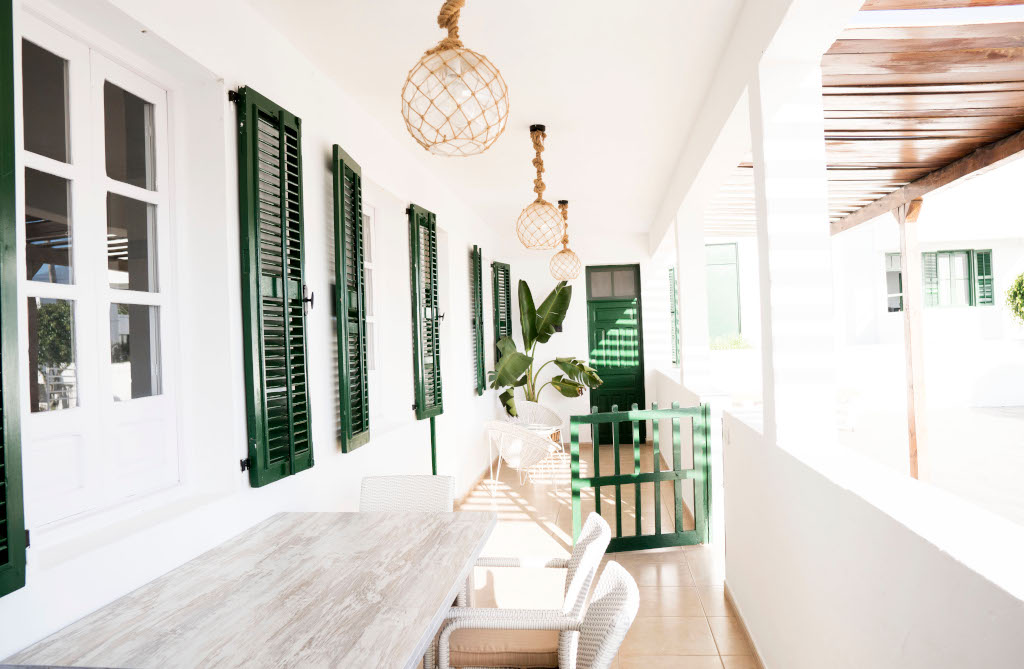 Terraza con mesa de madera y sillas, persianas y puertas verdes en Tenerife.