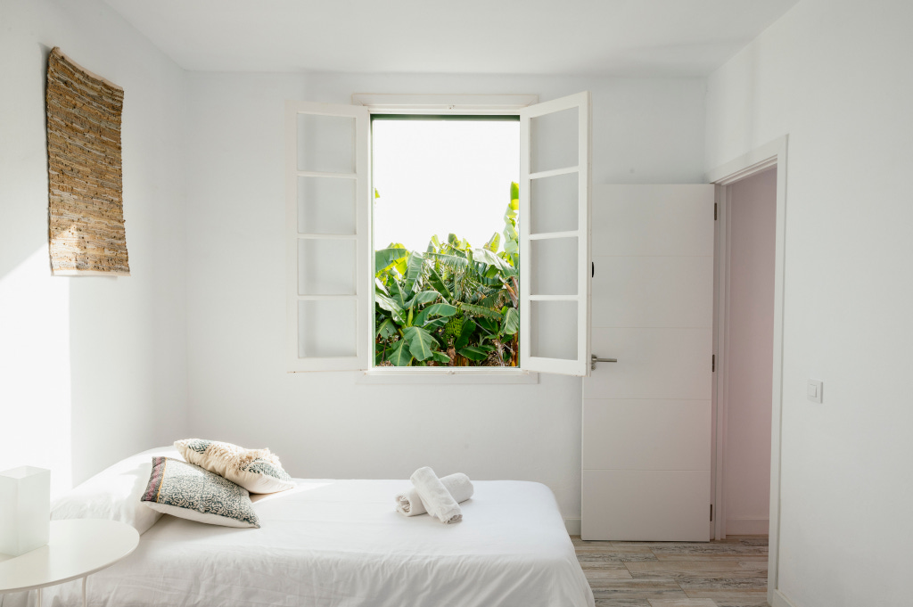 Habitación luminosa con cama sencilla y ventana abierta, vista exterior en Tenerife.