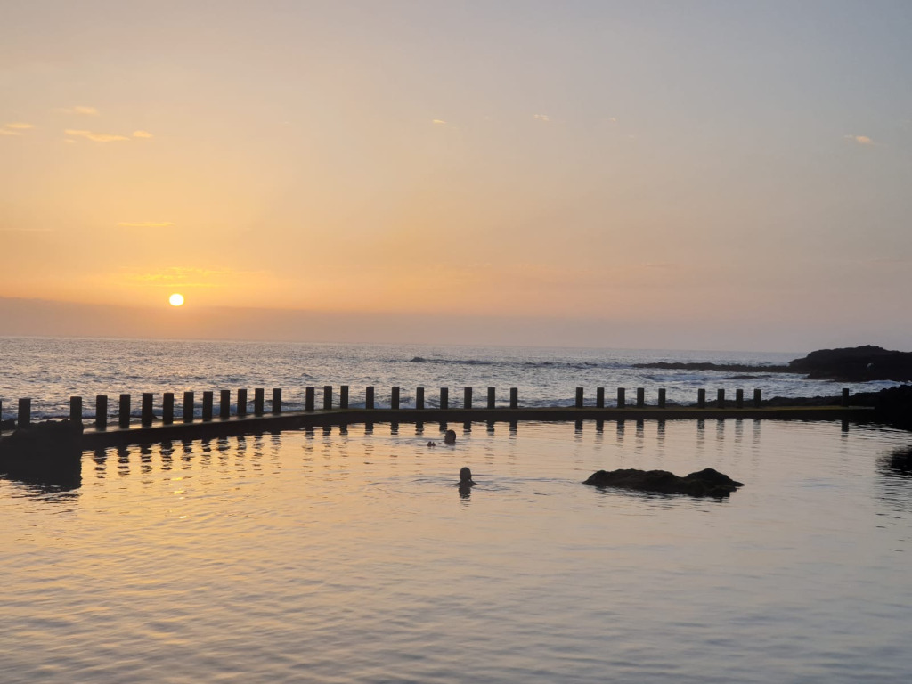 Puesta de sol en piscina natural de Tenerife con persona nadando.