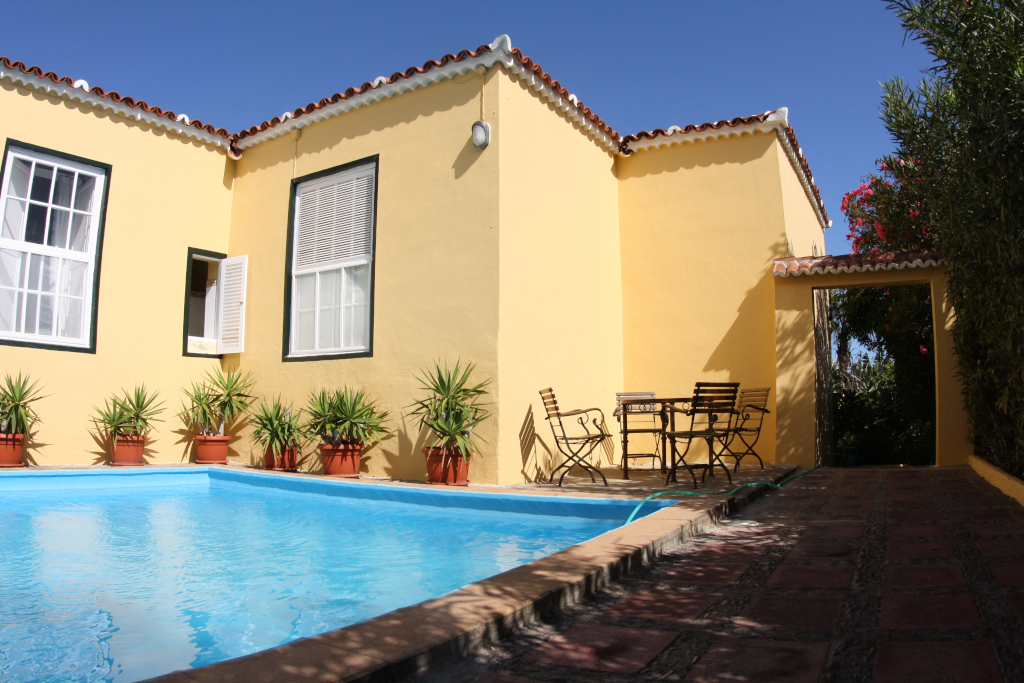 Piscina y patio con sillas al lado de una casa amarilla en Tenerife.