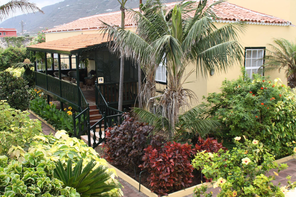 Casa en Tenerife rodeada de jardín con palmeras y arbustos coloridos.
