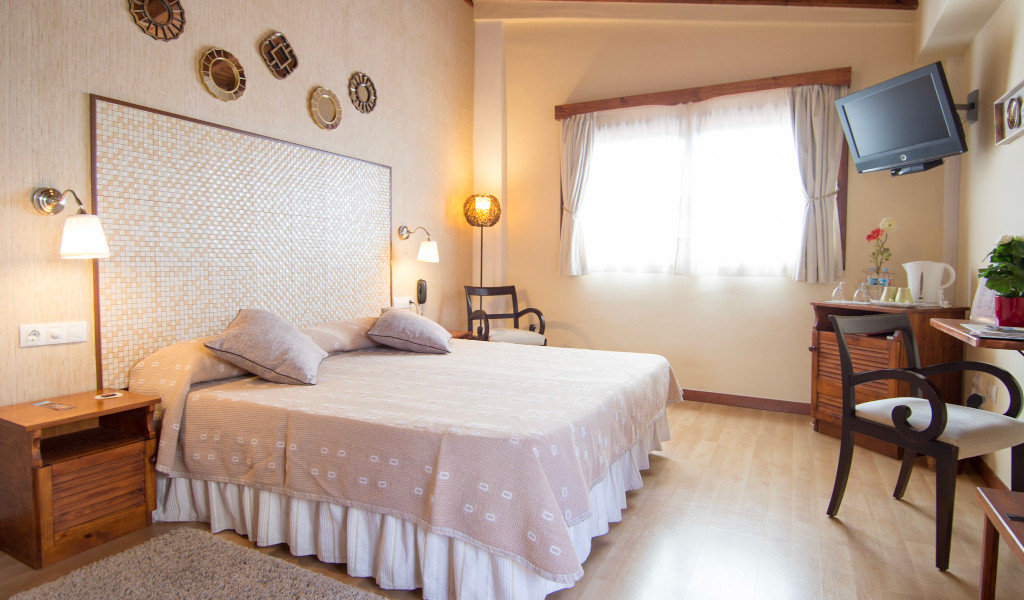 Habitación doble iluminada con cama amplia, televisor y muebles de madera en Tenerife.