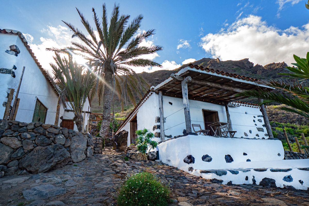 Casa rural con palmeras en Masca, Tenerife, bajo un cielo azul y montañas al fondo.