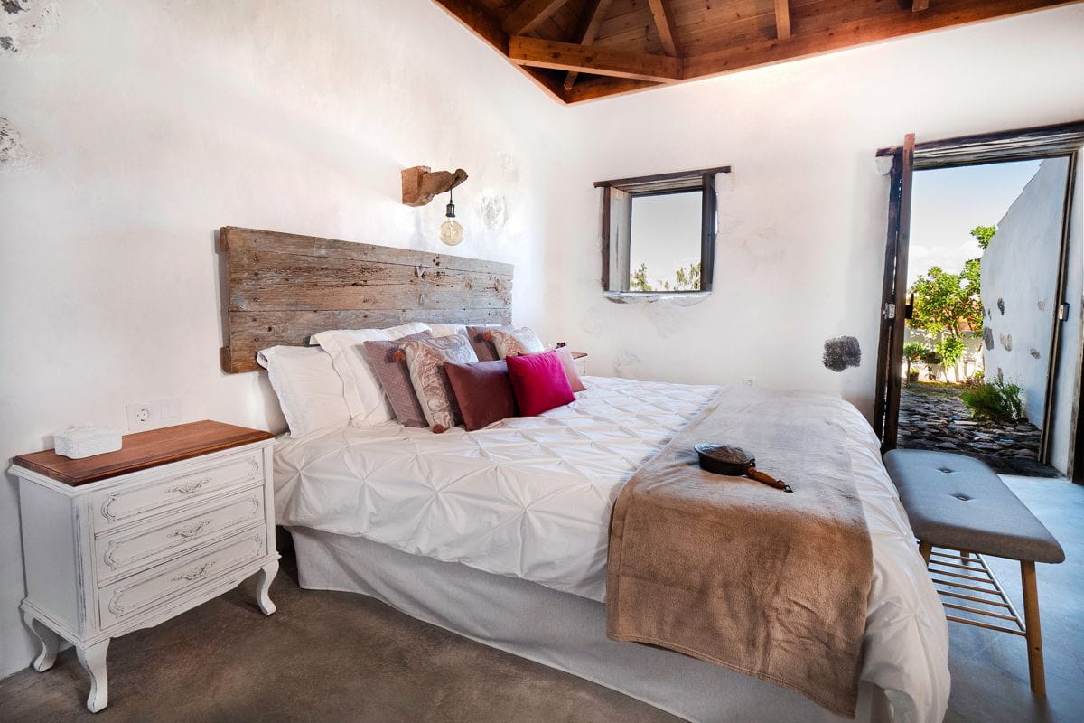 Cama con cabecero de madera y ventana abierta en habitación de Tenerife.