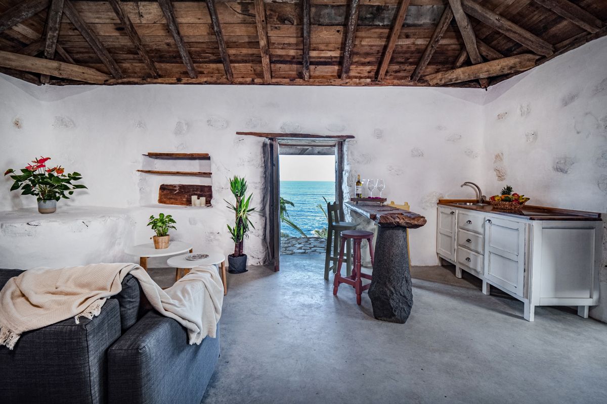 Sala rústica en Tenerife con techo de madera y vista al mar a través de la puerta.