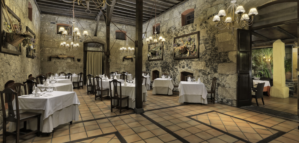 Restaurante en Tenerife con mesas vestidas y luces colgantes en un espacio rústico.