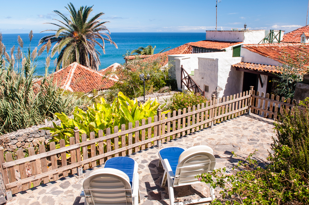Terraza con sillas y vista al mar en Tenerife, rodeada de plantas y palmeras.