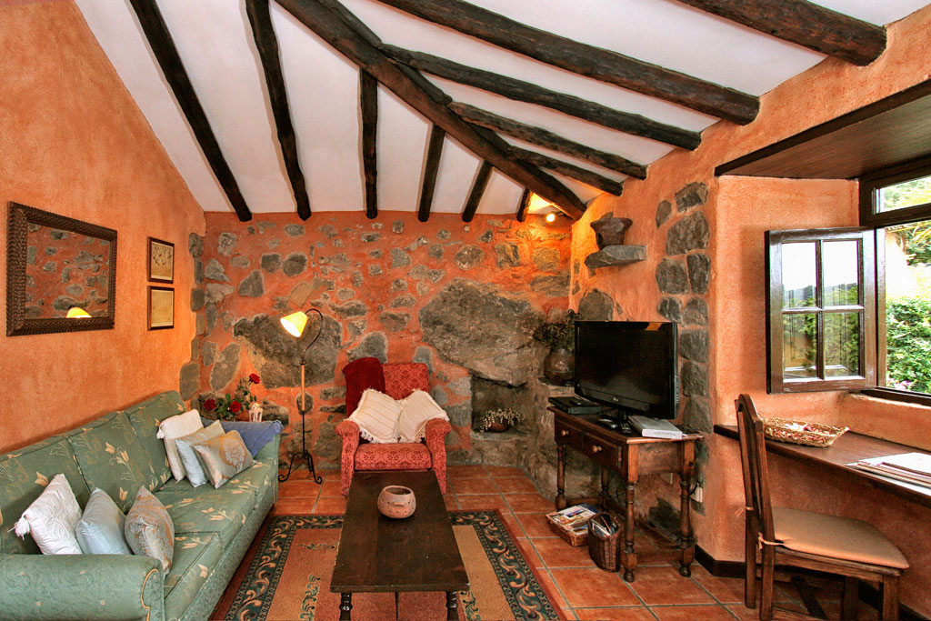 Sala de estar rústica con sofá, silla, televisor y ventana en Tenerife.
