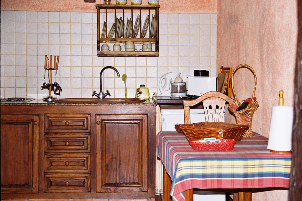 Cocina rústica con muebles de madera en Tenerife. Mesa con mantel a cuadros y vajilla.