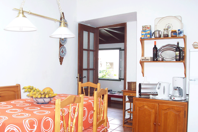 Comedor en Tenerife con mesa, sillas y estantería con electrodomésticos.