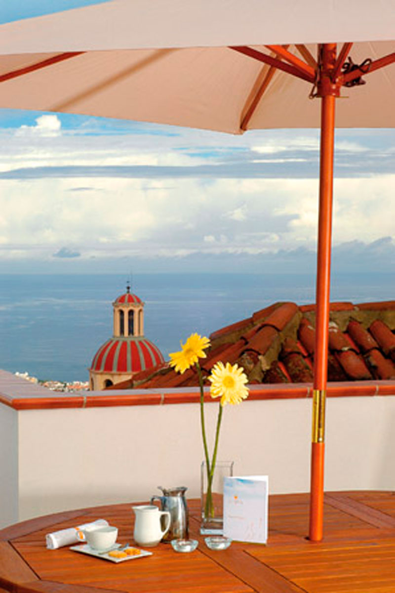Mesa con jarra de café, flores y menú, vista al mar y cúpula en Tenerife.