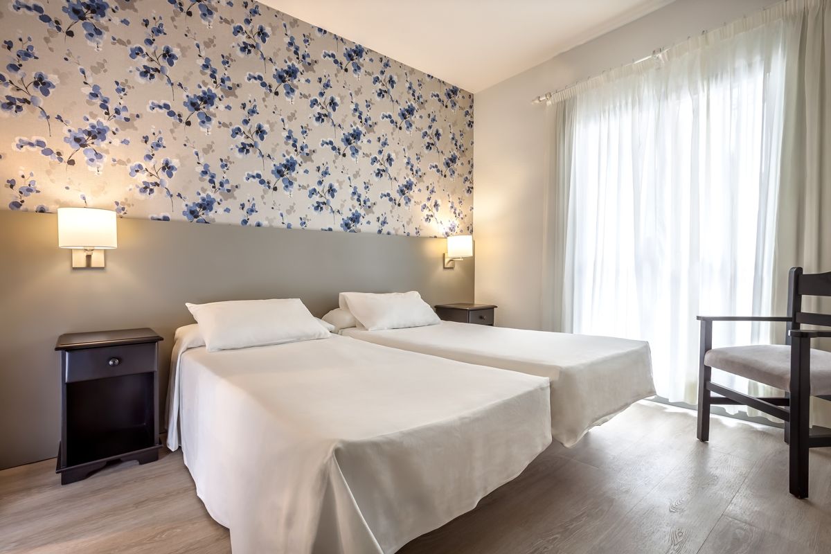 Dos camas individuales en habitación luminosa con papel tapiz floral en Tenerife.