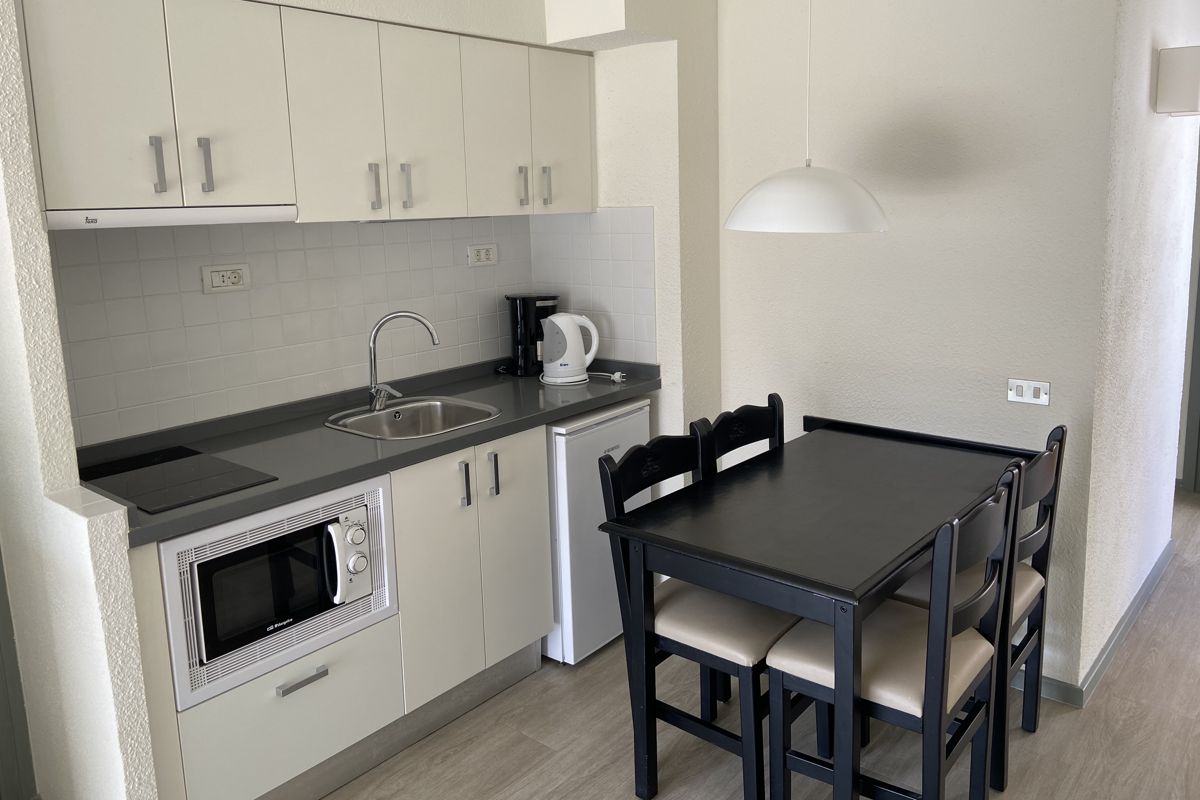 Cocina pequeña con mesa, sillas, microondas y fregadero en apartamento de Tenerife.