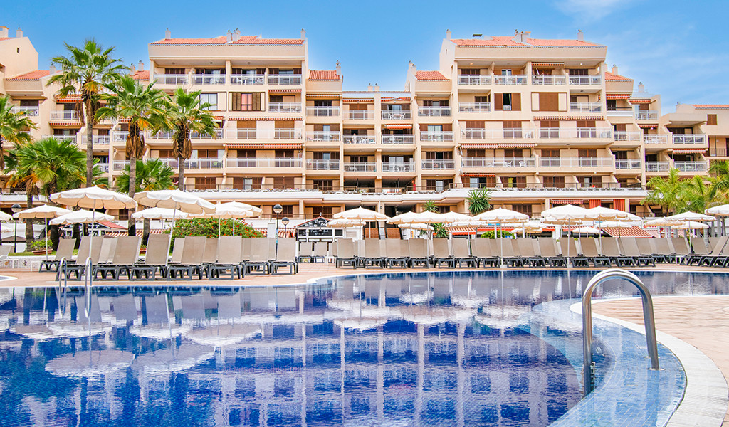 Piscina y hotel con palmeras en Los Cristianos, Tenerife.
