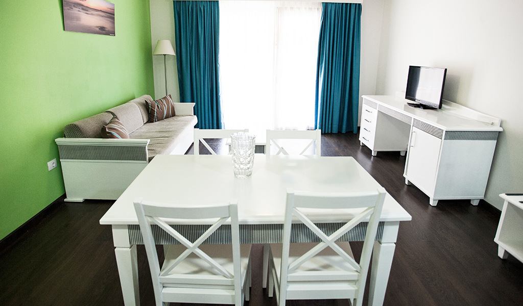 Sala de estar con mesa blanca, sofá, televisor y cortinas en un apartamento en Tenerife.