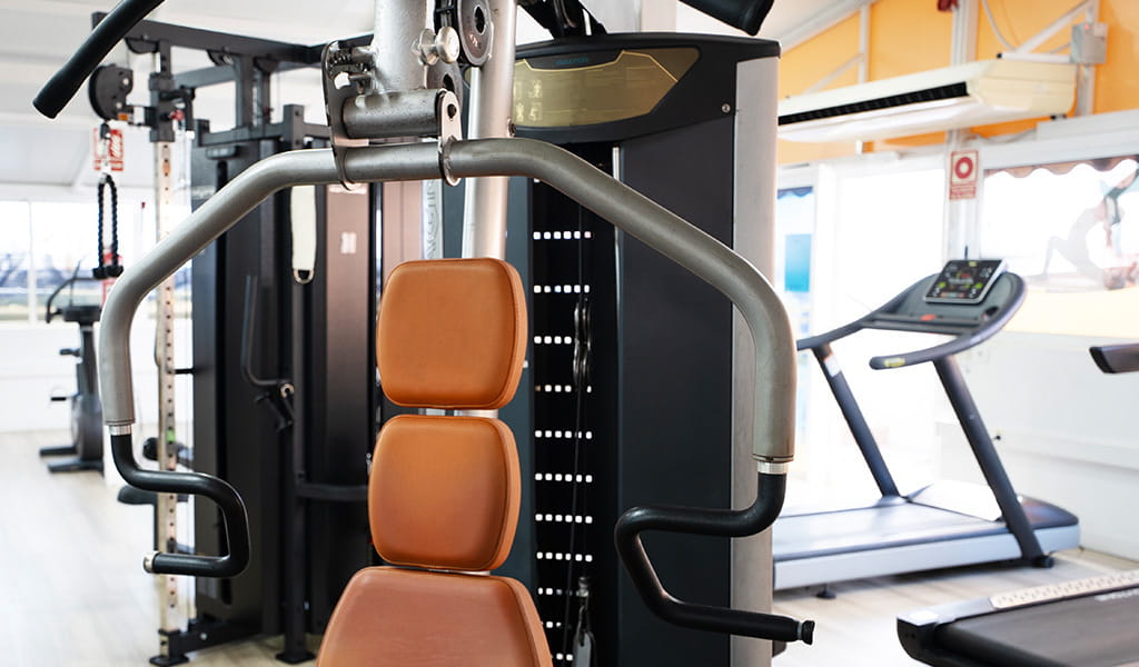 Máquina de ejercicios en gimnasio de Tenerife con cinta de correr al fondo.