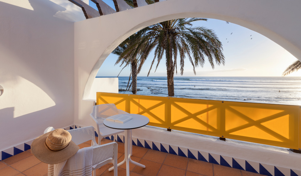 Terraza con mesa y sillas frente al mar en Tenerife, vista de palmeras y horizonte.