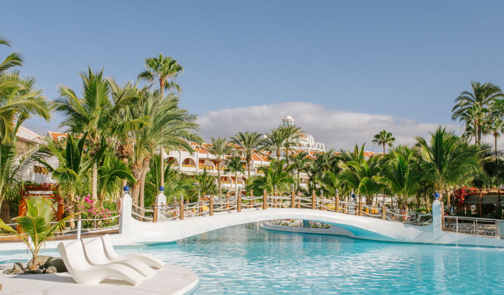 Piscina y puente rodeados de palmeras en complejo hotelero en Tenerife.