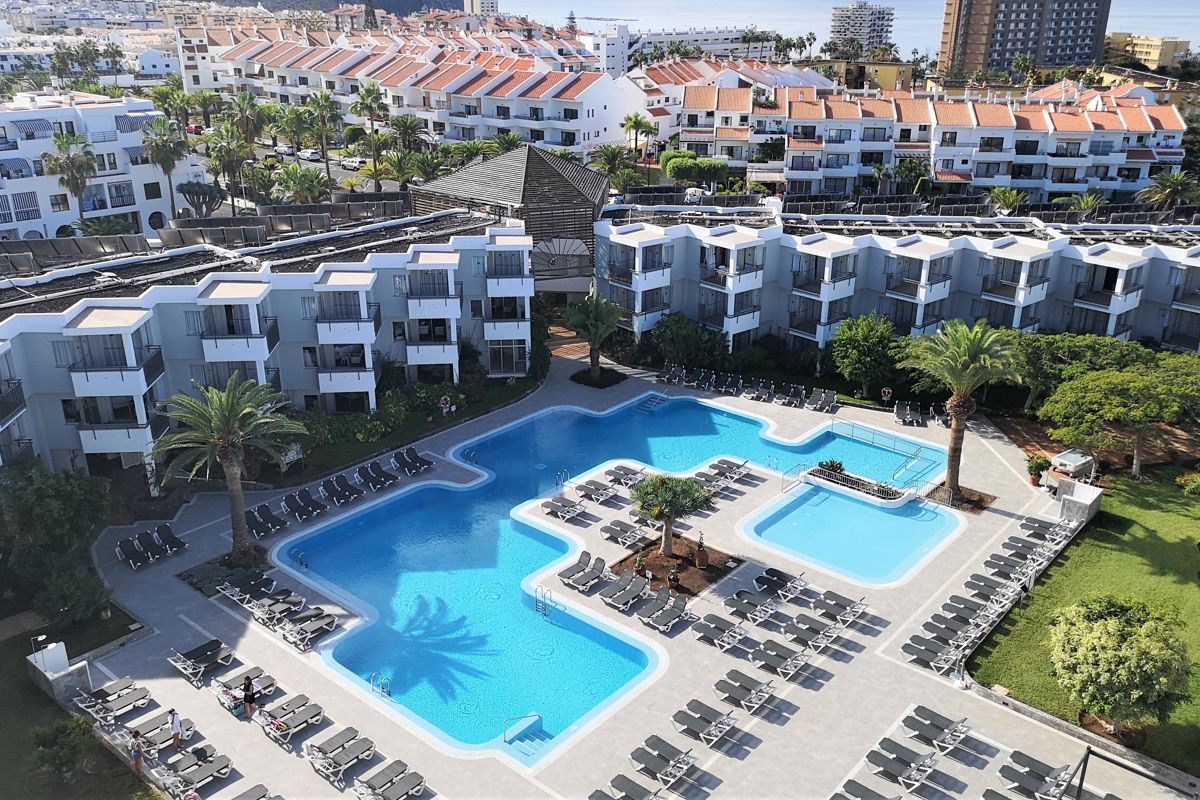 Piscina de un hotel rodeada de hamacas y edificios en Tenerife.