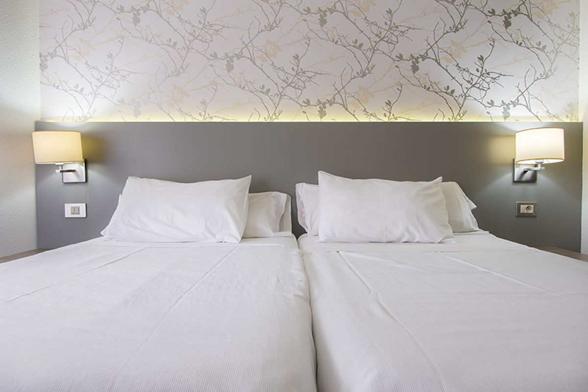 Camas dobles con cabecero gris y lámparas en hotel de Tenerife.