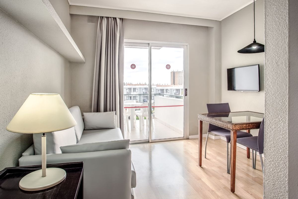 Sala de estar luminosa con sofá, televisión, mesa de comedor y balcón en Tenerife.
