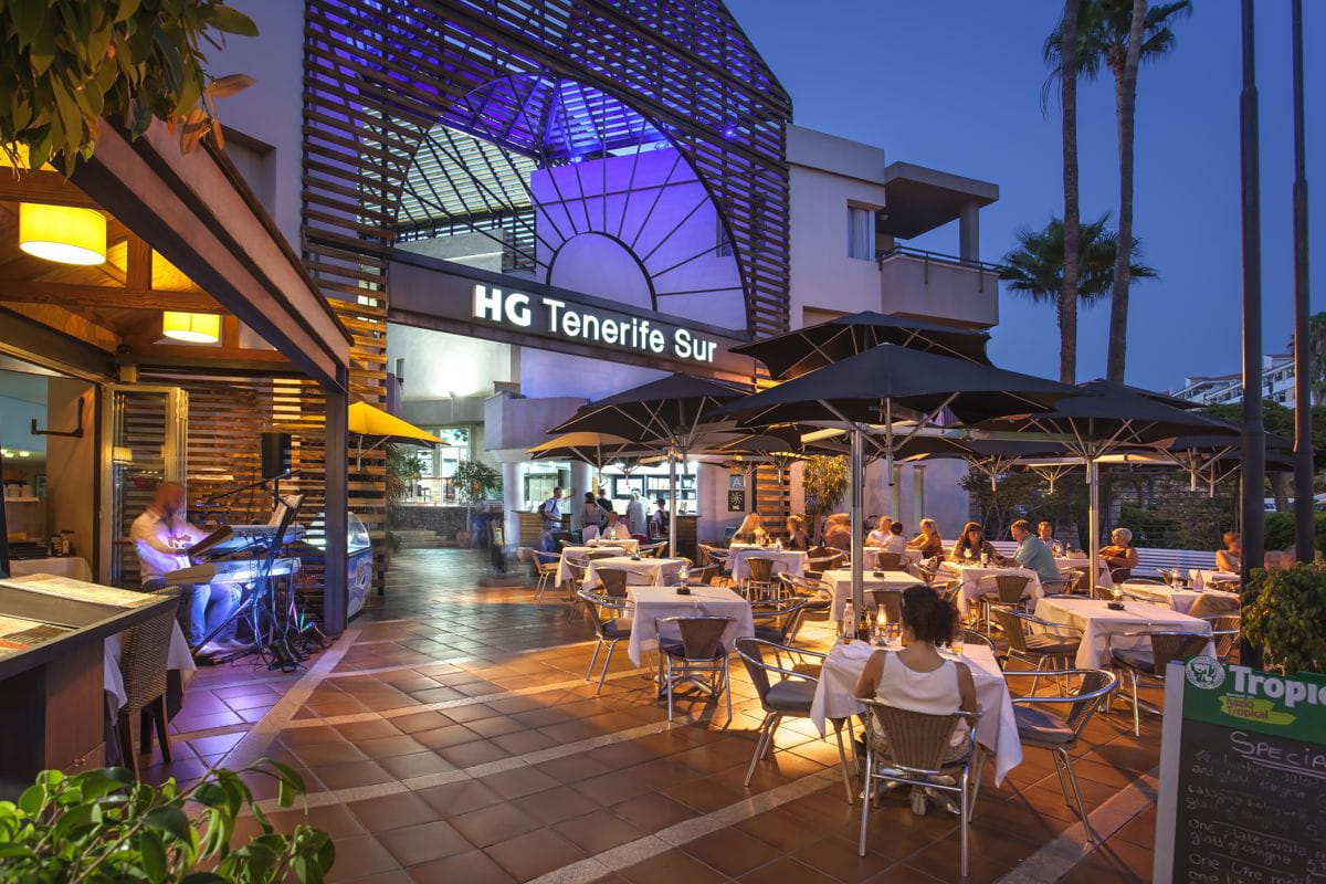 Terraza del restaurante en HG Tenerife Sur por la noche, con comensales cenando al aire libre.