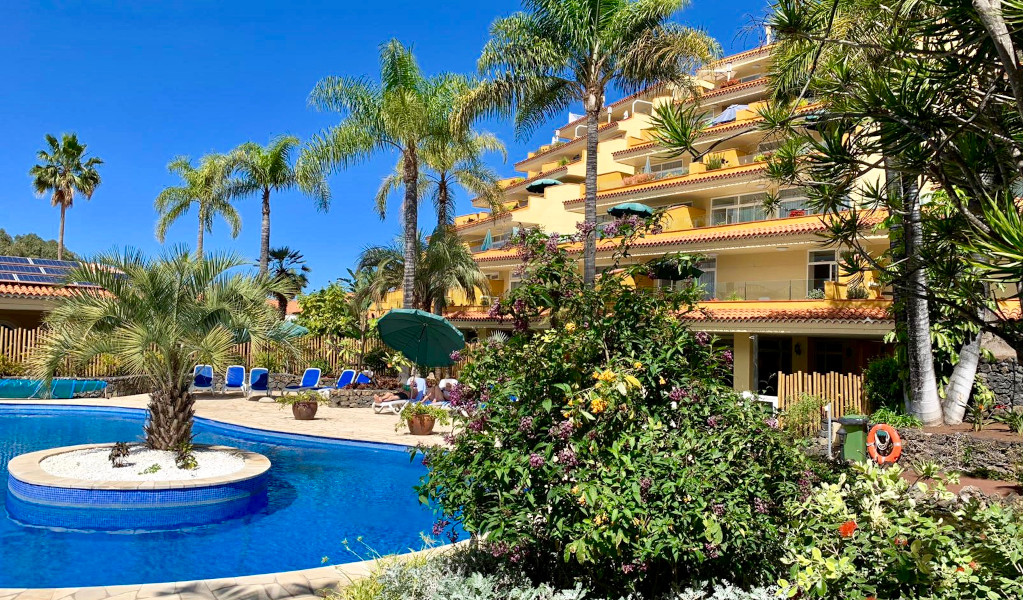 Piscina rodeada de palmeras y edificio de apartamentos en Tenerife.