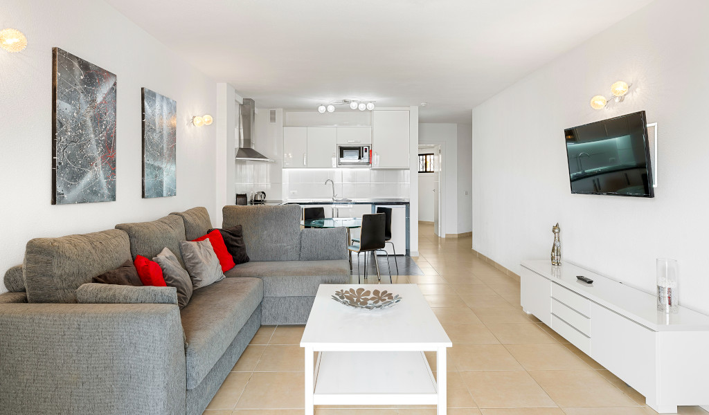 Sala de estar moderna en Tenerife con sofá gris y cocina integrada.