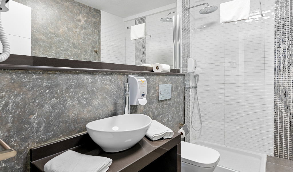 Baño moderno con lavabo, espejo, ducha y toallas en hotel de Tenerife.