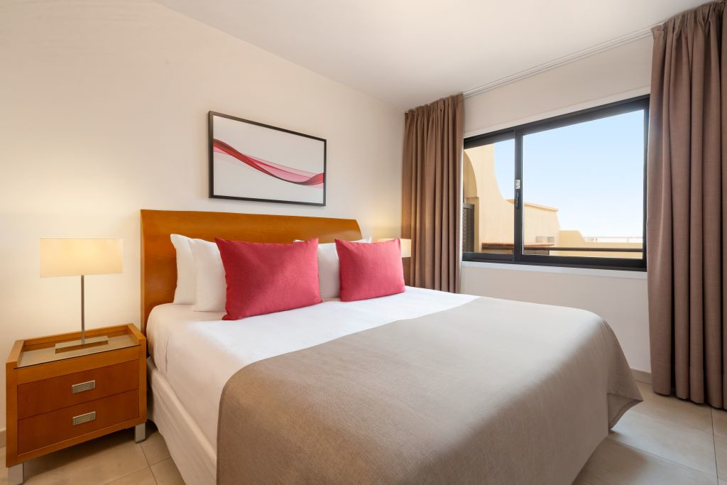 Habitación de hotel en Tenerife con cama doble, cojines rojos y ventana grande.