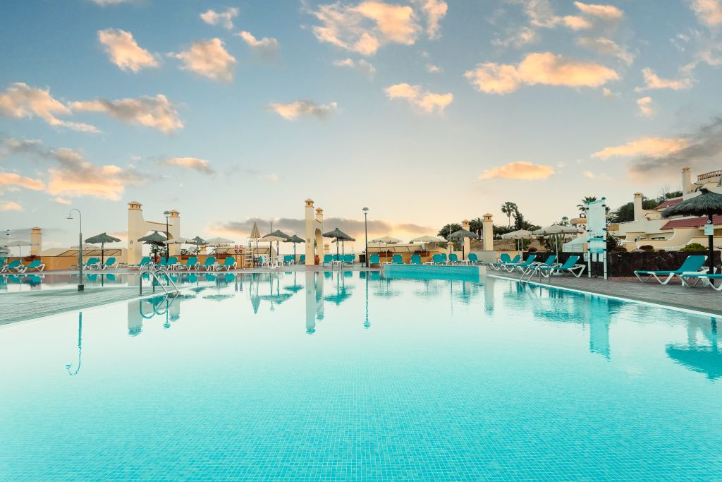 Piscina al aire libre al atardecer en Tenerife, rodeada de tumbonas y sombrillas.