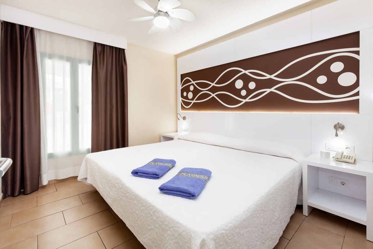 Cama doble con toallas azules y decoración en la pared en un hotel de Tenerife.