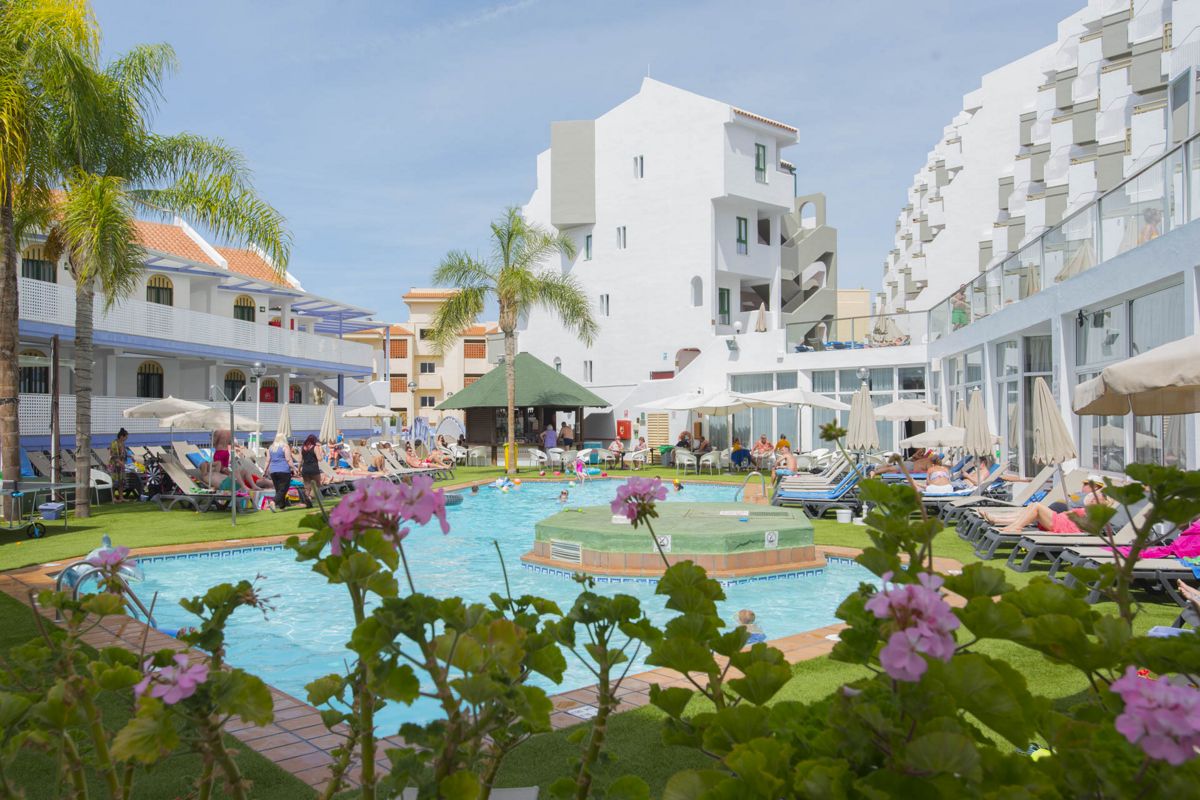 Piscina del hotel en Tenerife con huéspedes descansando y edificio de fondo.