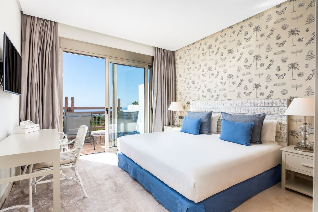 Habitación con cama doble, cojines azules y balcón con vistas al mar en Tenerife.