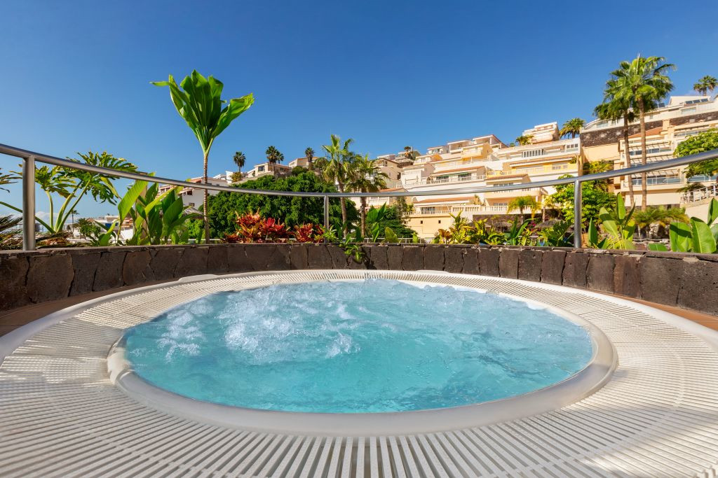 Jacuzzi rodeado de plantas con edificios en el fondo en Tenerife.